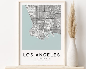 May include: A framed map print of Los Angeles, California, with a pale blue background. The map is in monochrome, showing city streets and the coastline. The text "LOS ANGELES CALIFORNIA" is printed below the map, along with the coordinates.