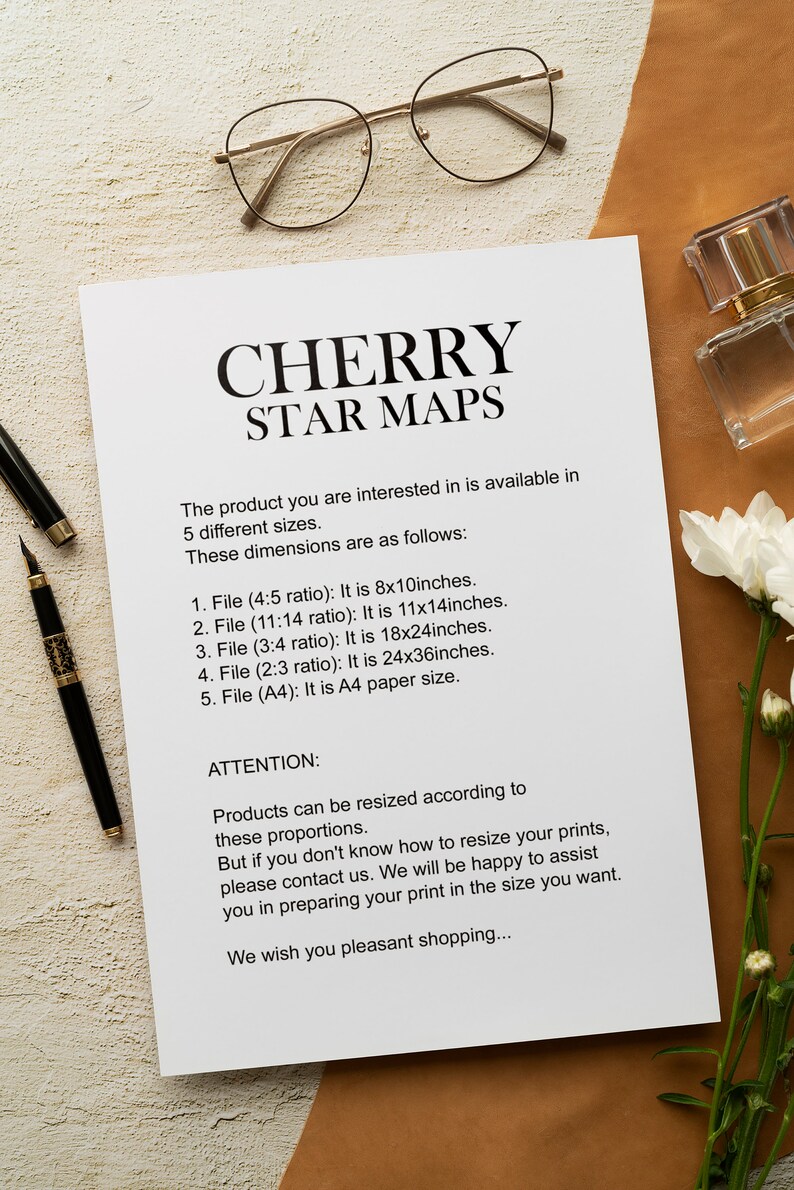 May include: A white sheet of paper with black text describing the different sizes available for a Cherry Star Map. The text includes the dimensions in inches and the aspect ratio of each size. The paper is on a brown surface with a pair of glasses and a bottle of perfume.