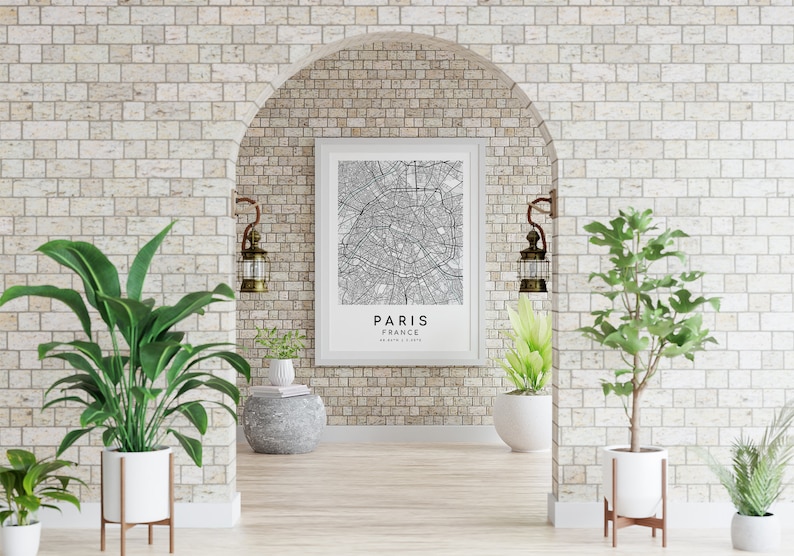 May include: A framed black and white map of Paris, France, hangs on a brick wall. The map is centered with the city name below. The room is decorated with plants in white pots and vintage-style lanterns.