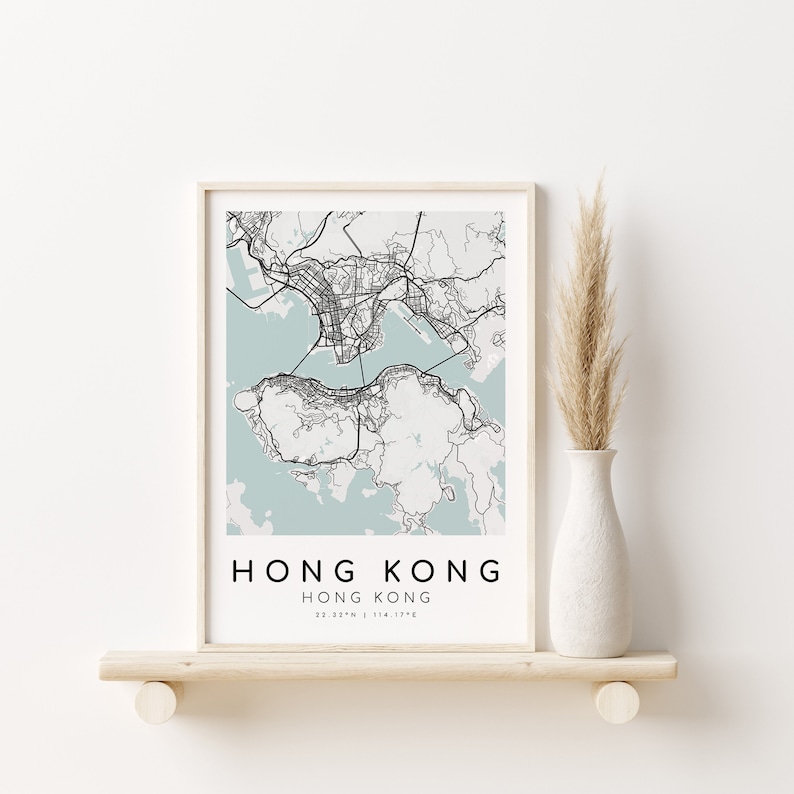May include: A framed map print of Hong Kong, featuring a detailed black and white city plan over a light blue background. The text "HONG KONG" is displayed in a clean font, with coordinates below. The print is displayed on a wooden shelf.