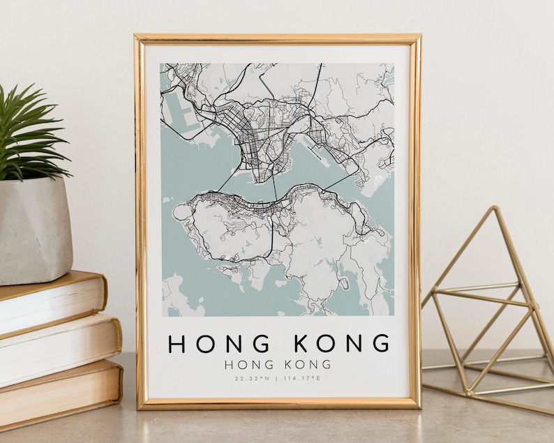 May include: A framed map print of Hong Kong, featuring a detailed black and white city plan against a light blue background. The text "HONG KONG" is displayed in a bold, sans-serif font, with coordinates below. The print is in a gold frame.