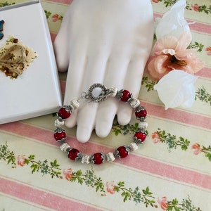 May include: A red bead bracelet with silver accents and a silver toggle clasp.