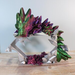 May include: A 3D printed crystal dragon figurine with iridescent green, purple, and pink colors. The dragon is curled up on a bed of white, gray, and purple crystals.