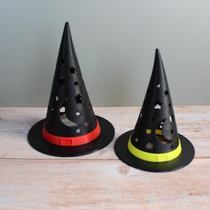 May include: Two black witch hats with star and crescent moon cutouts. One hat has a red band, the other a yellow band. Both have a wide brim and a pointed top, perfect for Halloween decorations.
