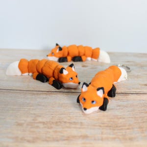 May include: Three orange and black fox figurines with white tails. The foxes are lying down with their heads turned to the side.