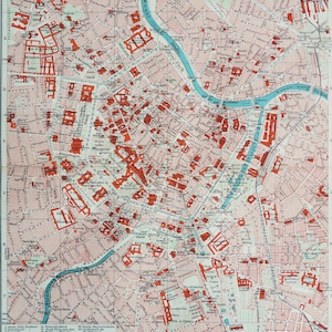May include: A vintage city map with a detailed street layout, buildings in red, and a blue river running through the center. The map has a grid system and text labels, likely for navigation.