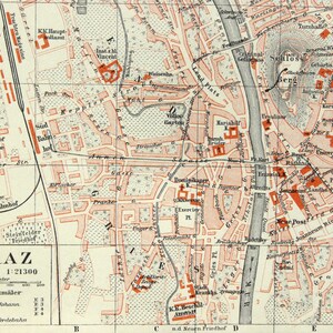 May include: Vintage map of Graz, Austria, showing streets, buildings, and the Schlossberg. The map uses beige and red tones, with German text. The scale is 1:21300.