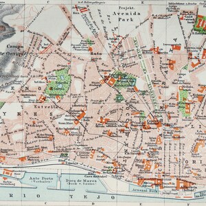 May include: A vintage printed map of Lisbon, Portugal, featuring a grid system, street names, and landmarks. The map displays urban areas in light beige, green parks, and orange buildings, with the Rio Tejo river at the bottom edge.