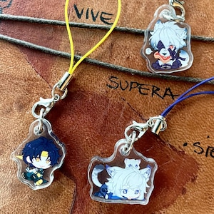 Op de afbeelding: Transparante acryl bedels met anime-achtige karakterontwerpen. Elke bedel heeft een ander personage met levendige kleuren en is bevestigd aan een koord. De bedels zijn verbonden met een metalen sluiting en een gekleurd koord. Het woord "VIVE" is zichtbaar.