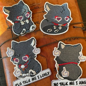 Può includere: Quattro toppe ricamate da stirare raffiguranti un gatto nero con occhi a forma di cuore rosso. Le toppe hanno testi diversi: "PLS TALK ME I LONLY", "NO TALK ME I ANG", e due toppe senza testo.