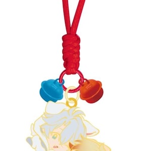 以下が含まれることがあります： 赤いコードのキーホルダー。ループがあり、金色のリングに青とオレンジの小さなベルが3つ付いています。下には、アニメ風の2人のキャラクターが愛情を込めて抱き合っている姿が描かれたチャームがあり、水色と黄色の髪をしています。