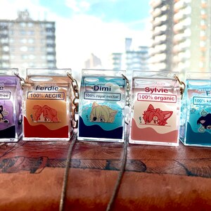 May include: Five colorful milk carton-shaped keychains with different character illustrations and names. The keychains are made of clear plastic with glitter inside. The characters are Hubie, Ferdie, Dimi, Sylvie, and Feli.