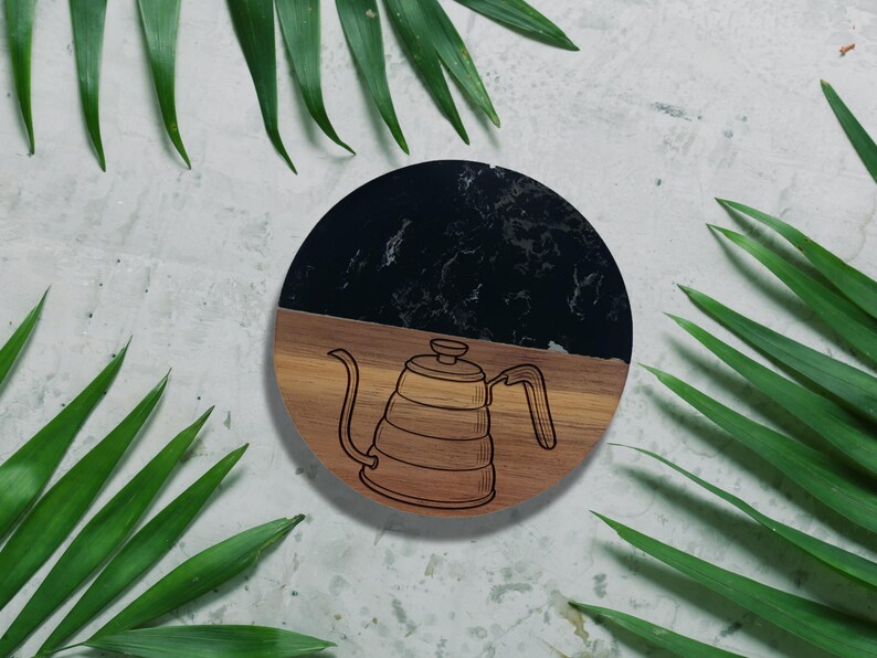 a wooden coffee pot with a black handle, surrounded by green leaves on a white background.