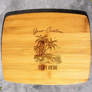 May include: A natural bamboo cutting board with a laser engraved design of palm trees and a beach scene. The text "Your Custom Text Here" is also engraved on the board.