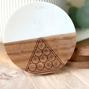 May include: A round coaster with a white and wood grain design. The bottom half of the coaster is wood, with a laser-etched pool ball rack design. The top half is white with a marble-like pattern. Numbers 1, 3, 4, 5, 6, 11, 12, and 15 are visible.