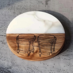 May include: A round wooden coaster with a half-circle of white marble and a half-circle of wood. The wooden portion features a detailed engraving of two bongo drums. The coaster is designed for use with beverages.