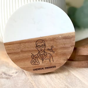 May include: A round coaster with a white and wood grain design. The wood grain section features a line drawing of a chemical engineer with the text "CHEMICAL ENGINEER". The coaster is made of wood and resin.
