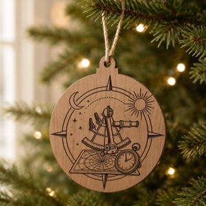 May include: Wooden Christmas ornament with a nautical theme. The round ornament features a compass rose, a sextant, a clock, a sun, a moon, and stars. The ornament is hanging from a natural twine string.