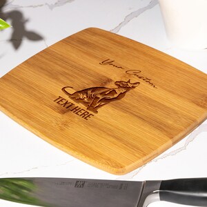 May include: A personalized bamboo cutting board with a laser-engraved image of a cat and the text "Your Custom Text Here".