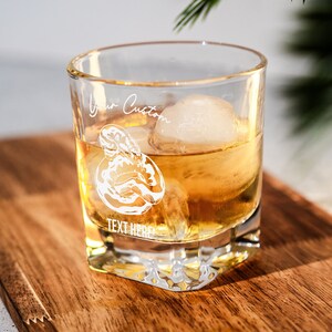 May include: A clear glass rocks glass with a white design of a lobster and the text "Your Custom Text Here". The glass is filled with amber liquid and an ice cube.