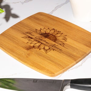 May include: A personalized bamboo cutting board with a sunflower design and the text "Your Custom Name".