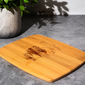 May include: A rectangular bamboo cutting board with a laser-engraved design of a beach scene with a pier, sun, and birds. The text "Your Custom Text Here" is engraved on the board.
