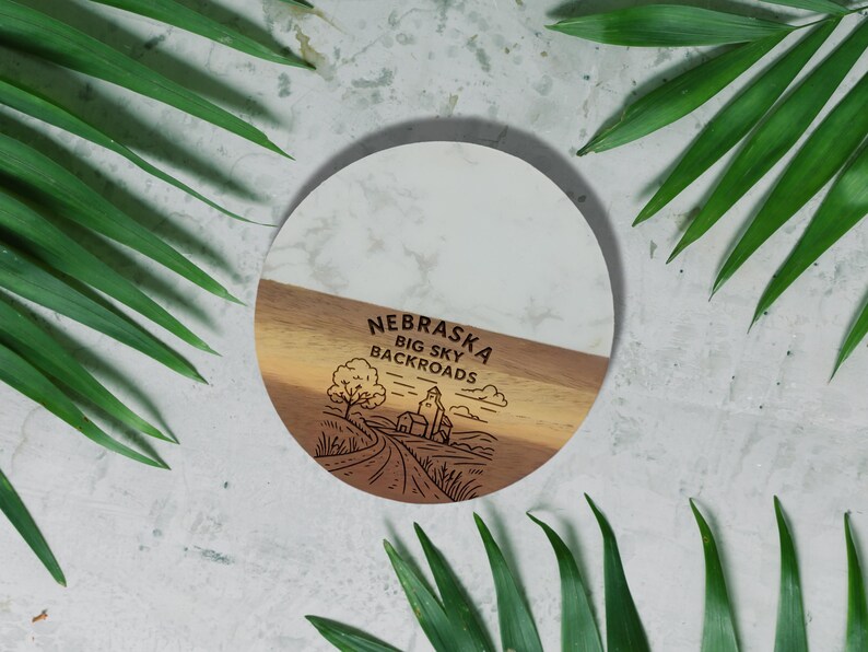 a round wooden coaster with a design depicting a road and a tree, surrounded by green leaves.
