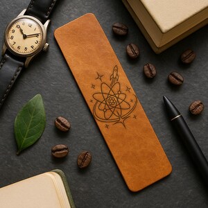 a leather bookmark with an intricate design, a watch, a pen, and coffee beans arranged on a dark surface.