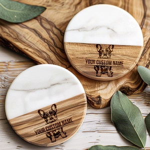 May include: Two round coasters made of white marble and wood. The top half of each coaster is white marble and the bottom half is wood. Each coaster has a French Bulldog silhouette and the text "YOUR CUSTOM NAME" engraved on the wood.