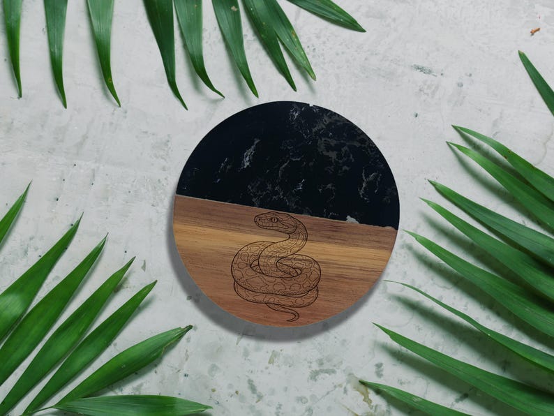 a round wooden tray with a black and brown design, surrounded by green leaves.