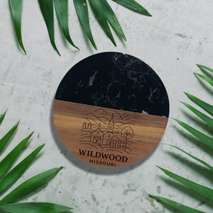 a round wooden coaster with a black marble top, surrounded by green leaves.