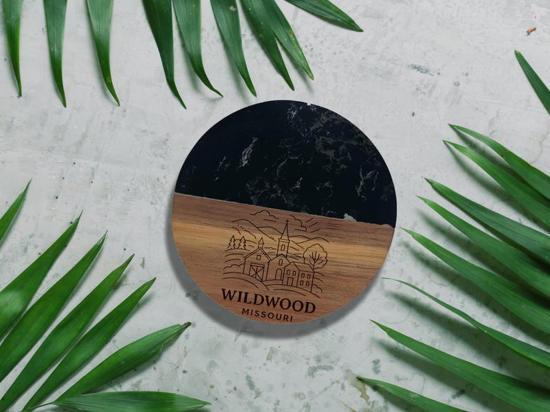 a round wooden coaster with a black marble top, surrounded by green leaves.