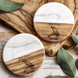 May include: Two round coasters made of white marble and wood. The wood portion of each coaster has a laser-engraved parrot design and the text "Your Custom Text Here".