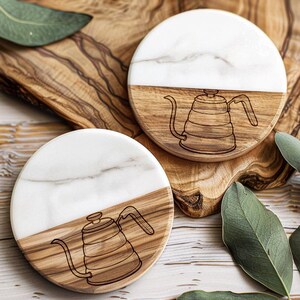 two round coasters with a wooden design and a white marble pattern, placed on a wooden surface with some leaves.