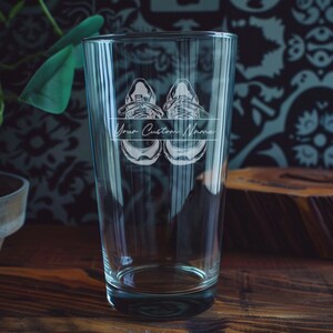 May include: A clear glass beer mug with a design of two sneakers and the text "Your Custom Name" etched on the side.