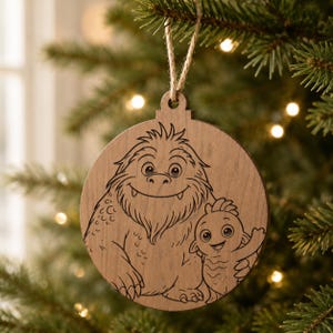 May include: A wooden Christmas ornament with a laser-etched design of two friendly cartoon creatures. The ornament is round with a natural wood finish and a jute string for hanging. The design features a large, furry monster and a smaller, fish-like character.