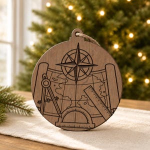 May include: Wooden Christmas ornament with a nautical theme. The ornament is round with a compass rose, map, and drafting tools etched into the wood. A jute string is attached for hanging. The ornament is brown.
