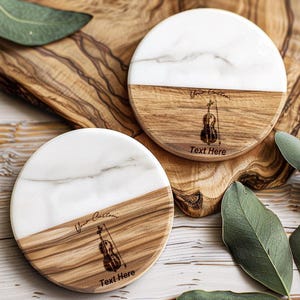 May include: Two round wooden coasters with a white marble top. Each coaster has a laser engraved violin design and the text "Your Custom Text Here".