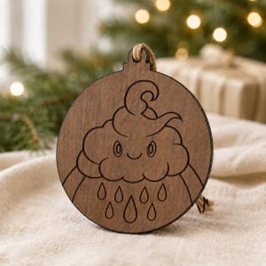 May include: Wooden Christmas ornament with a cloud design and raindrops. The ornament is round with a natural wood finish and a jute string for hanging. The cloud has a smiling face.