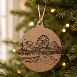 A wooden ornament hanging on a Christmas tree, featuring an illustration of a ferris wheel and a pier.
