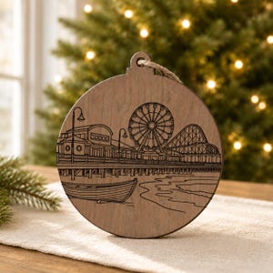 A wooden ornament featuring an illustration of a ferris wheel and a pier, with a Christmas tree in the background.