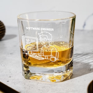 May include: A clear glass tumbler with a white graphic of a software engineer at a computer, the words "SOFTWARE ENGINEER" are above the graphic. The glass is filled with a golden liquid. A small coffee cup is next to the engineer.