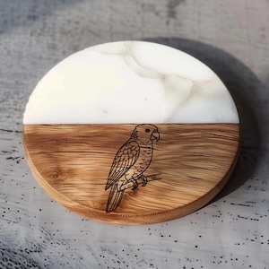 May include: A round coaster with a two-tone design. The top half is white with a marbled effect, and the bottom half is wood-grained. A black outline of a parrot is etched into the wood. The coaster is approximately 4 inches in diameter.