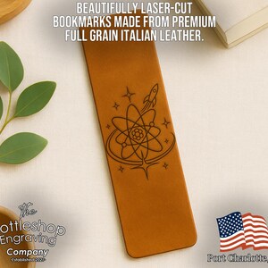 a brown leather bookmark with an intricate design, including a rocket ship and a flower, and a small American flag. The bookmark is placed on a white surface, with a plant and a book visible in the background.