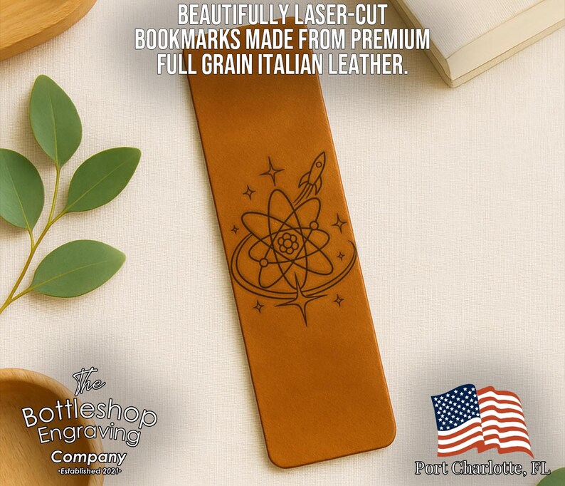 a brown leather bookmark with an intricate design, including a rocket ship and a flower, and a small American flag. The bookmark is placed on a white surface, with a plant and a book visible in the background.