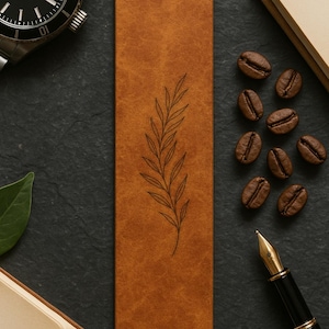 May include: A brown leather bookmark with a delicate leaf design. The bookmark is rectangular and lies on a dark surface, surrounded by coffee beans, a pen, and a watch. The overall aesthetic suggests a theme of reading and coffee.