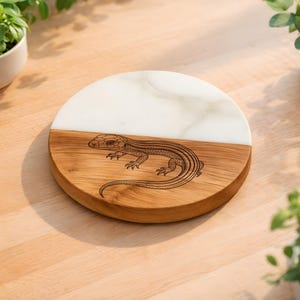 May include: Round wooden and white marble serving board. The wooden section features a detailed etched lizard design. The board is approximately 8 inches in diameter. Decorative and functional for serving appetizers or displaying items.