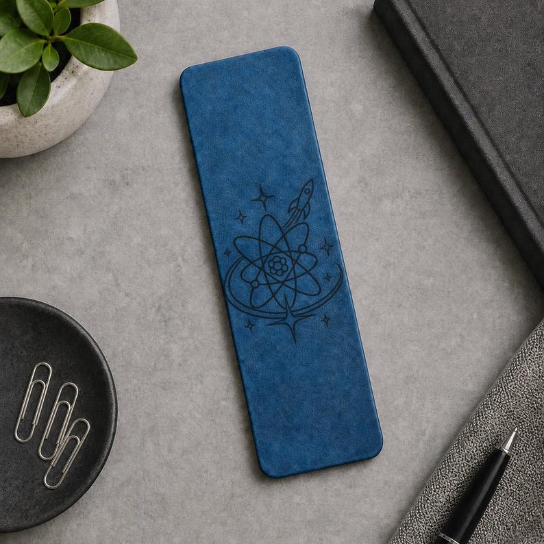 a blue notebook with a space-themed design, a black pen, a black pen holder, a black plate with silverware, a black plant, and a black book.