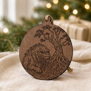 May include: A round, wooden Christmas ornament with a detailed engraving of a creature and a tree. The ornament is brown with a natural wood grain and a jute string for hanging. The creature has a stern expression.