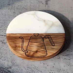 A wooden coaster with a white and brown design featuring a coffee pot.